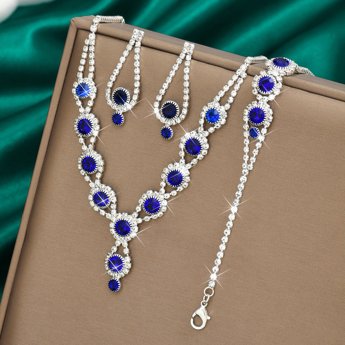 Royal blue rhinestone necklace, earrings and bracelet on green satin